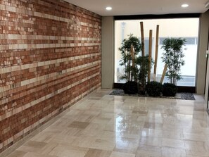 A lobby with a brick wall, a tiled floor, and indoor plants. - Beautiful apartment with sea view - 4 guests (Les Sables-d'Olonne)