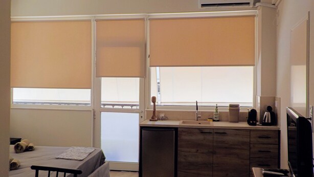 Een kleine hotelkamer met een bed, een bureau, een kitchenette en een raam met zonwering.