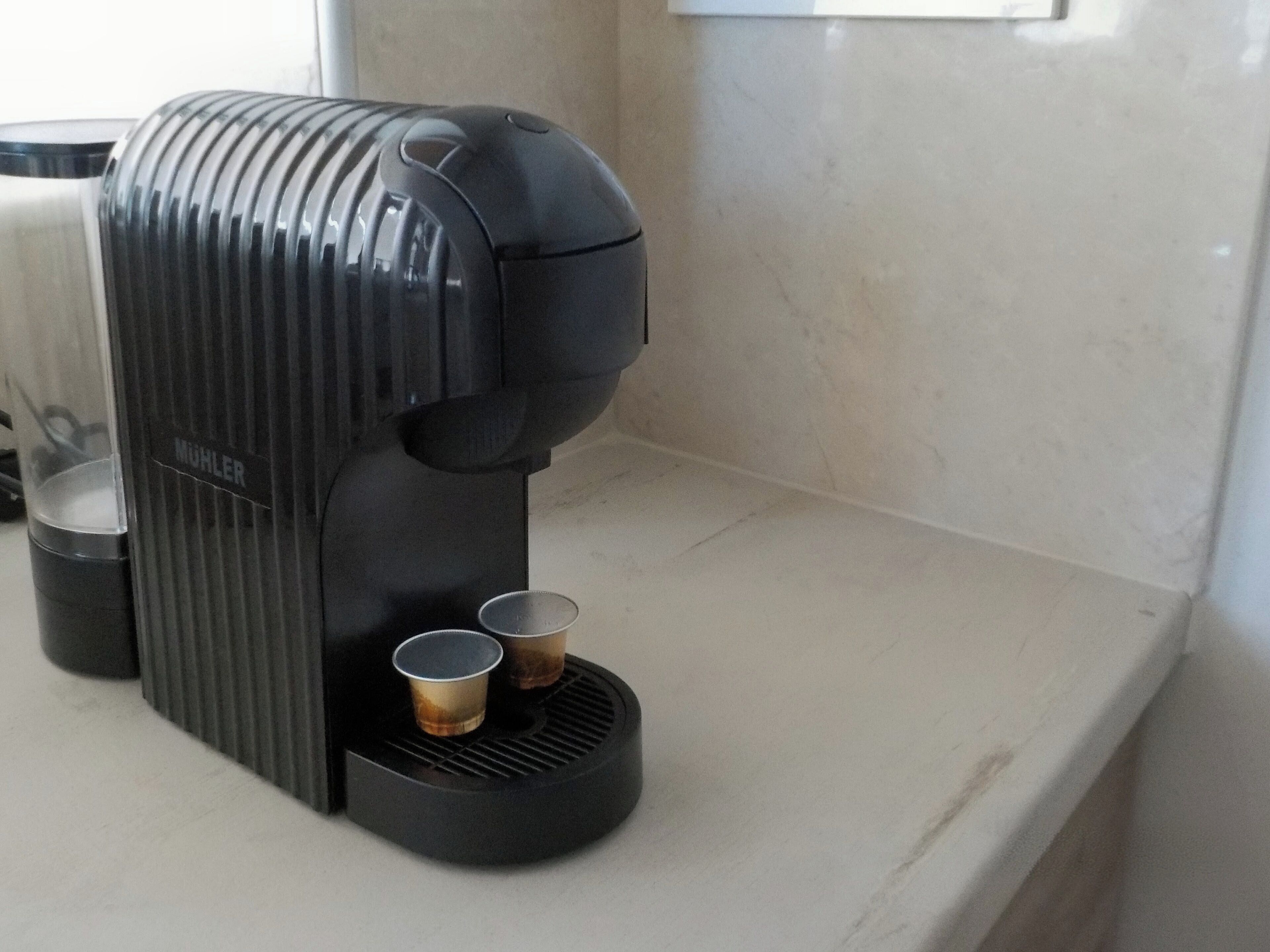 A coffee maker with two paper cups on a countertop.