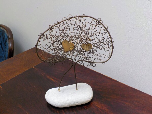 A metal sculpture resembling a tree with heart-shaped leaves on a white base, placed on a wooden table.