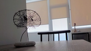 Een kamer met een houten tafel, een stoel, een decoratief metalen beeldhouwwerk en een raam met jaloezieën.