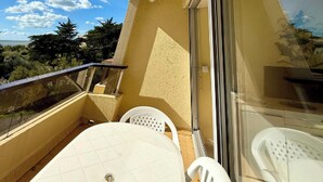 Un balcon avec une table et des chaises, une porte vitrée et une vue sur les arbres et le ciel.