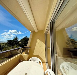 Ein Balkon mit Tisch und Stühlen, einer Glastür und Blick auf Bäume und den Himmel.