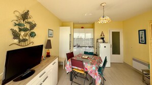 Un espace de vie compact comprenant un coin repas, une kitchenette et un téléviseur posé sur un meuble en bois.