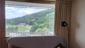Una habitación con vistas a un paisaje verde a través de una ventana, un sofá con cojines y una lámpara en la pared.