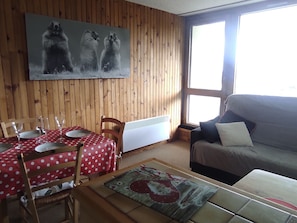A room with a dining table set with plates and glasses, a sofa, a radiator, and a painting of bears on the wall. - Comfortable studio, 4 guests, Super Besse center (Besse-et-Saint-Anastaise-Super Besse)