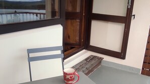 Un balcón con una mesa, dos tazas rojas, una silla y vistas a un lago.