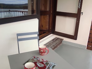 A balcony with a table, two red mugs, a chair, and a view of a lake. - Comfortable studio, 4 guests, Super Besse center (Besse-et-Saint-Anastaise-Super Besse)