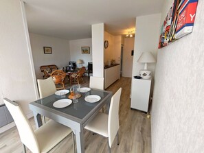 A dining area with a table set for four, a kitchen in the background, and a living area with wicker furniture. - T3 Apartment with parking, sea & mountain view (Canet-en-Roussillon)