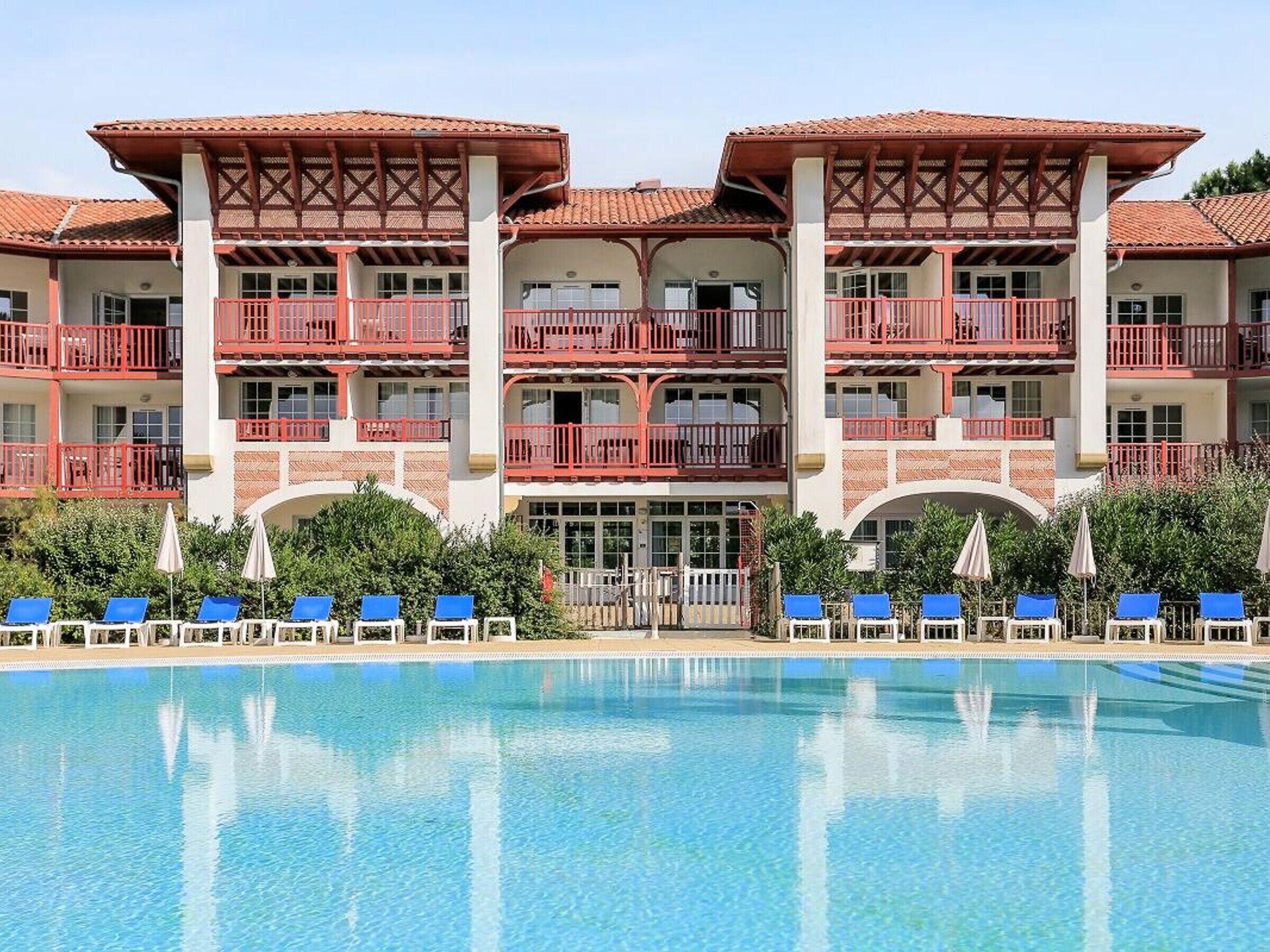 A hotel with a large pool, multiple balconies, and blue lounge chairs.