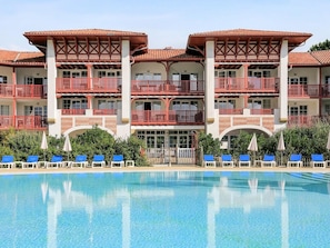 Ein Hotel mit großem Pool, mehreren Balkonen und blauen Liegestühlen.