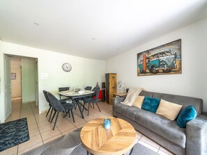 Ein Wohnzimmer mit grauem Sofa, einem runden Holztisch, einem Esstisch mit Stühlen, einer Uhr und einem Gemälde eines Oldtimers.