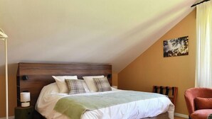 Une chambre à coucher avec un lit, des oreillers, une lampe de chevet, une chaise et un tableau au mur.