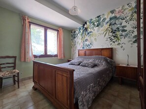 A bedroom with a wooden bed, a chair, a nightstand, a window with curtains, and a floral wallpaper. - Residential house, pets on request - 4 guests (Grues)