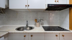 A kitchen with white cabinets, a stainless steel sink, and a black stove. - Seafront apartment, Wi-Fi included (Torredembarra)