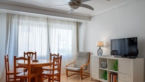 A dining area with a round table and chairs, a ceiling fan, a television on a cabinet, and a bookshelf. - Seafront apartment, Wi-Fi included (Torredembarra)