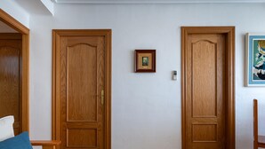 A room with two wooden doors, a framed picture on the wall, a small table, and a blue cushion on a sofa. - Seafront apartment, Wi-Fi included (Torredembarra)
