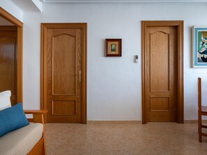 A room with two wooden doors, a framed picture on the wall, a small table, and a blue cushion on a sofa. - Seafront apartment, Wi-Fi included (Torredembarra)