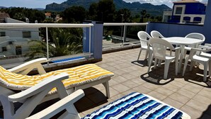 Eine Dachterrasse mit Liegestühlen, einem Tisch und Stühlen, mit Blick auf Berge und die Stadt.