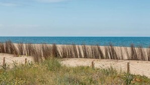 Ein Strand mit Sandfläche, Holzzaun und blauem Himmel.