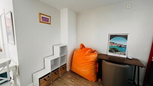 A room with a white wall, a wooden floor, a white chair, a small table with a picture, and a bean bag chair. - Apartment near the beach - 4 guests (Argelès-sur-Mer)