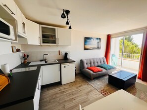 Een moderne keuken met witte kastjes, een zwart aanrecht en een zithoek met een grijze bank en een kleine tafel.