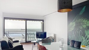 Una sala de estar moderna con una mesa de vidrio, sillones de cuero, un televisor y un ventanal grande con vista al océano.