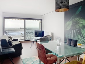 Ein modernes Wohnzimmer mit Glastisch, Ledersesseln, Fernseher und einem großen Fenster mit Meerblick.