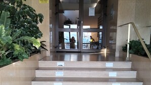 Unos escalones beiges conducen a una puerta de cristal con una entrada, donde se ve a una persona afuera.