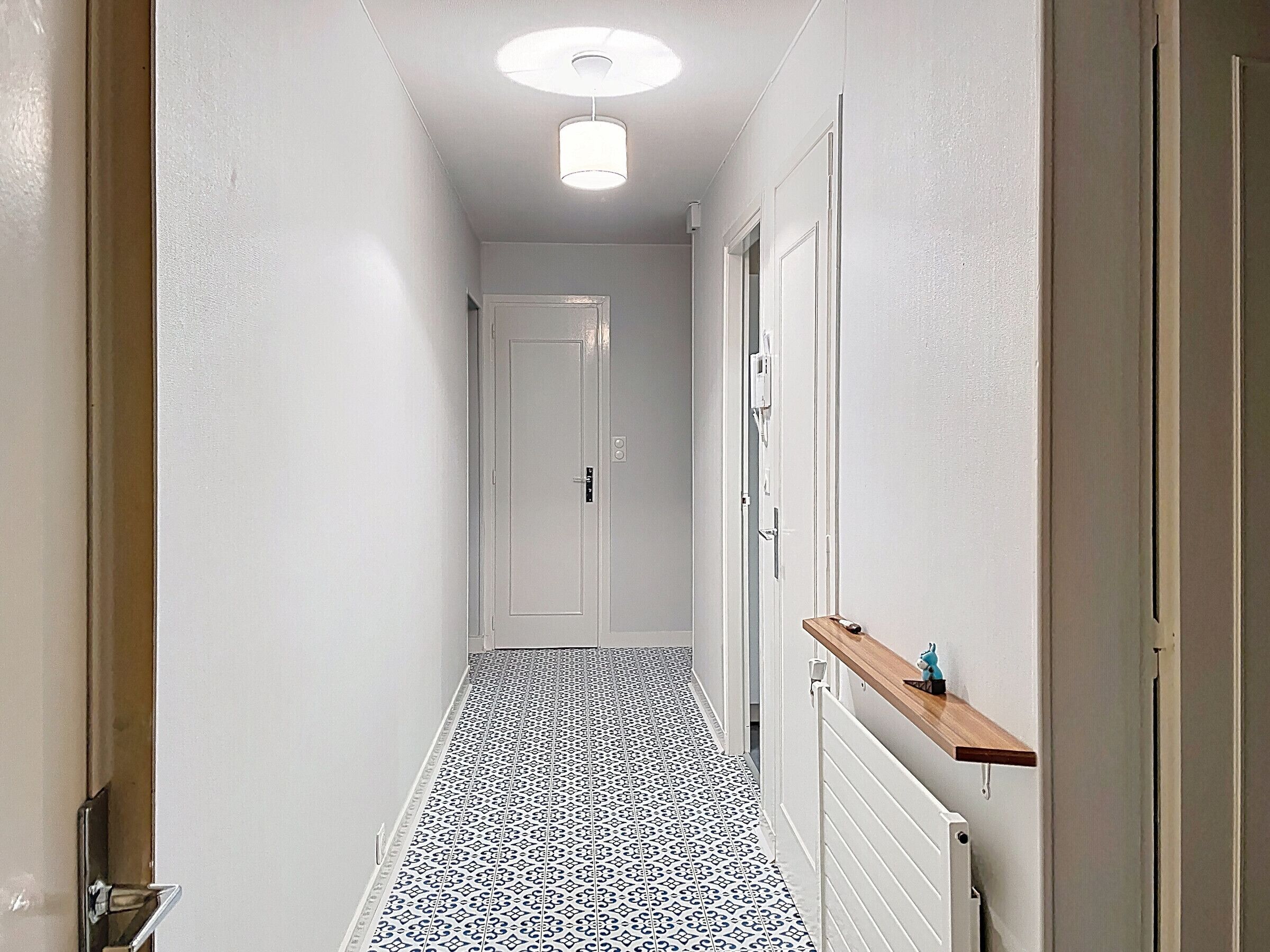 A narrow hallway with patterned flooring, white walls, and a ceiling light fixture.