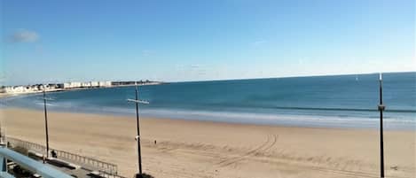 A beach view with a clear sky, a sandy shore, and a distant coastline.