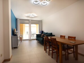 Ein Essbereich mit Tisch und Stühlen, einer Couch und Blick durch eine Glastür auf einen Außenbalkon.