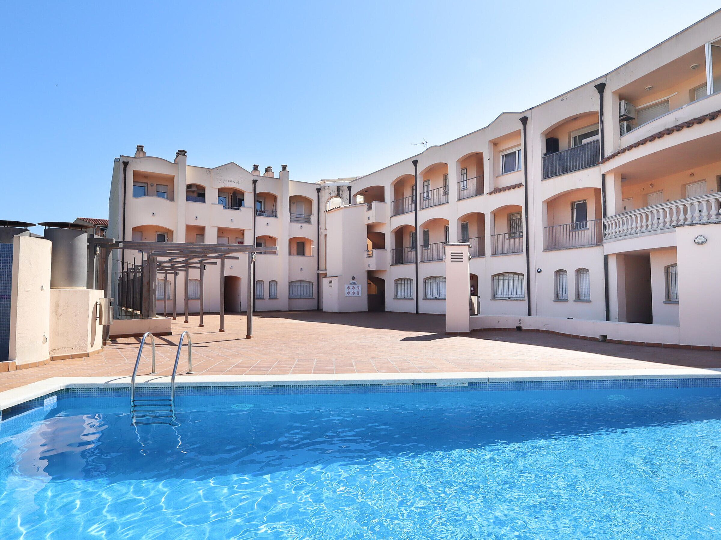 A swimming pool with a metal ladder, surrounded by a multi-story building with balconies and a tiled roof.