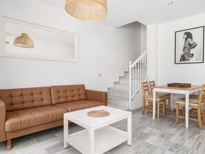 Ein modernes Wohnzimmer mit einer braunen Ledersofa, einem weißen Couchtisch, einem Esstisch mit Stühlen, einer Treppe und einem gerahmten Kunstwerk an der Wand.