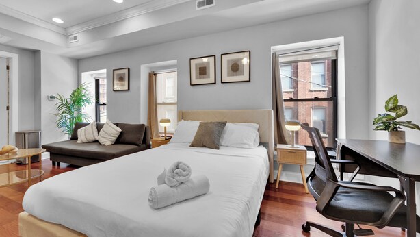 Ein modernes Hotelzimmer mit einem großen Bett, einem Schreibtisch, einem Sessel, einem kleinen Tisch und einer Zimmerpflanze.