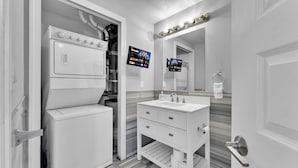 Ein modernes Badezimmer mit integrierter Waschmaschine und Trockner, einem Waschtisch mit Spiegel und zwei flachbildschirmigen Fernsehern an der Wand.