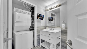 A modern bathroom with a built-in washer and dryer, a vanity with a mirror, and two flat-screen TVs mounted on the wall. - Apartmint at 1149E N 3rd St Philadelphia (Philadelphia)