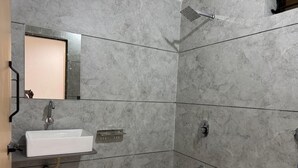 Un baño con lavamanos blanco, espejo, ducha y piso de baldosas.