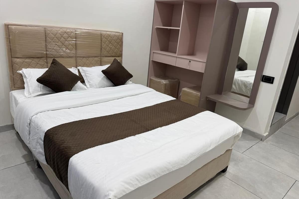 Uma cama com cabeceira, almofadas, mesa de cabeceira, espelho e guarda-roupa.