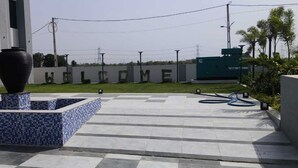 Un patio con piso de baldosas, un jarrón decorativo grande y un edificio con un letrero que dice 'WELCOME'.