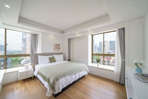 Un dormitorio con una cama grande, una mesita de noche, una ventana con cortinas y vistas a edificios.