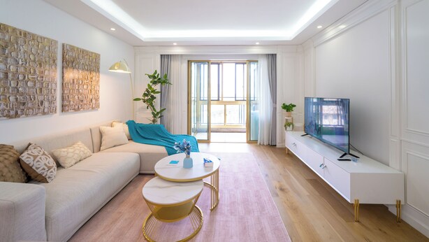 En moderne stue med sofa, sofabord, fjernsyn og et stort vindue med gardiner.