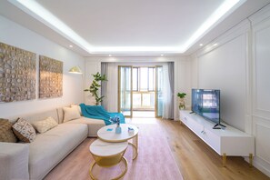 Una sala de estar moderna con un sofá, una mesa de centro, un televisor y un ventanal con cortinas.