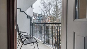 Ein Balkon mit Metallstühlen, einem schwarzen Metallgeländer und Blick auf Gebäude und Bäume.