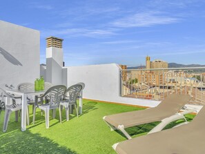 Una terrassa al terrat amb taula i cadires, un petit barbacoa i vista a la ciutat.