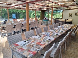 Un área de comedor al aire libre cubierta con sillas y mesas de mimbre, una parrilla y vistas a árboles.