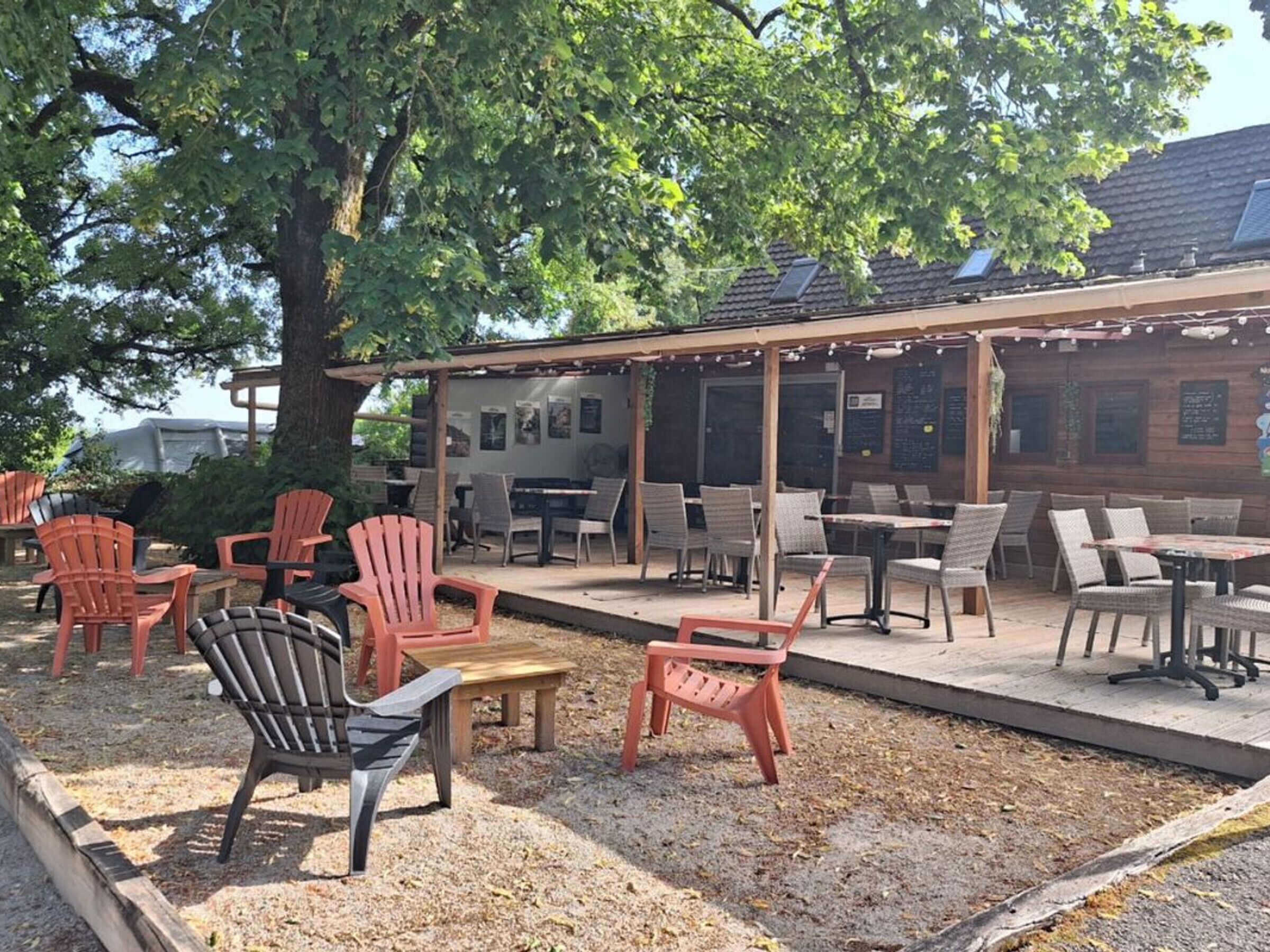 Un espacio al aire libre con sillas Adirondack y mesas, un pérgola y un edificio con tejado de baldosas.