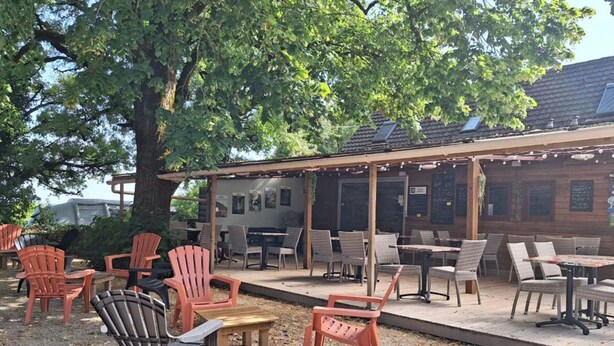 Un espace extérieur aménagé avec des chaises Adirondack et des tables, une pergola et un bâtiment doté d’un toit en tuiles.