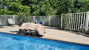Piscina com água cristalina, uma formação rochosa e uma cerca branca.