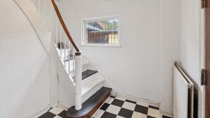 Un escalier aux murs blancs, un sol à carreaux noirs et blancs et une fenêtre donnant sur les bâtiments environnants.